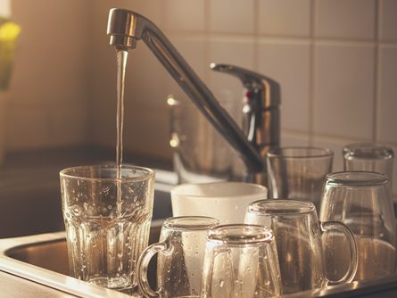 주방 싱크대 위에 놓인 다양한 크기의 물컵들과 수도꼭지, 물방울이 맺힌 투명한 유리컵